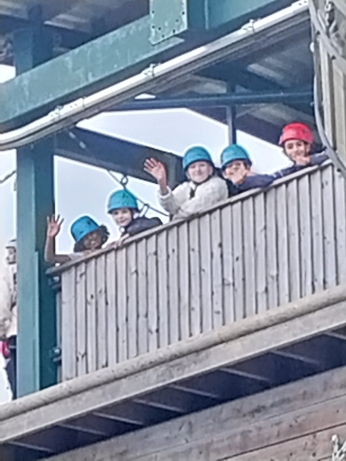 Mixed group of children waving from on top of the zip wire tower