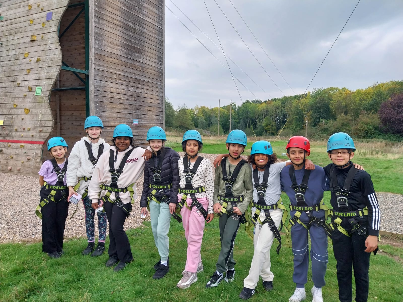 Mixed group of children in a line smiling for a photo in front of the zip wire tower
